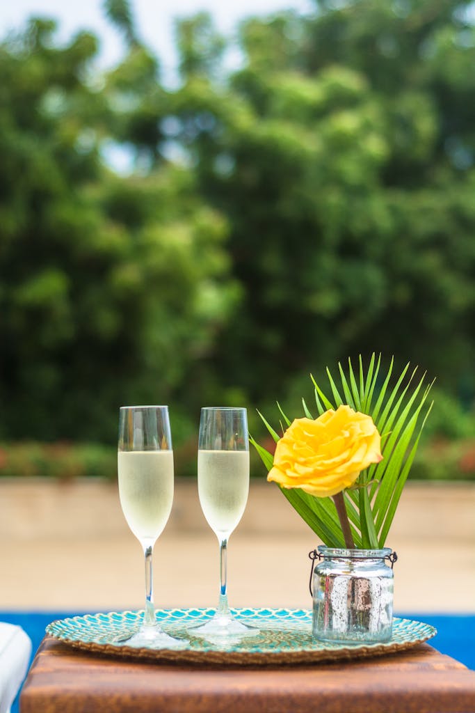 Two champagne glasses with a yellow rose on a table, evoking a sense of celebration.
